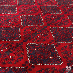 A close-up of a red patterned rug with dark navy blue geometric and floral motifs outlined in white.